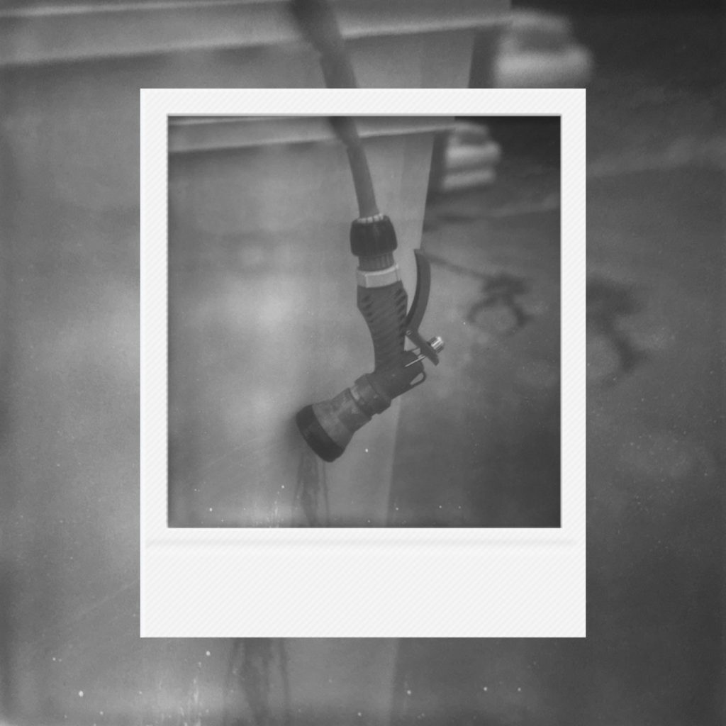 A peaceful afterimage of daily life frozen in coarse monochrome film textures featuring a hose hanging quietly where motion once dwelled