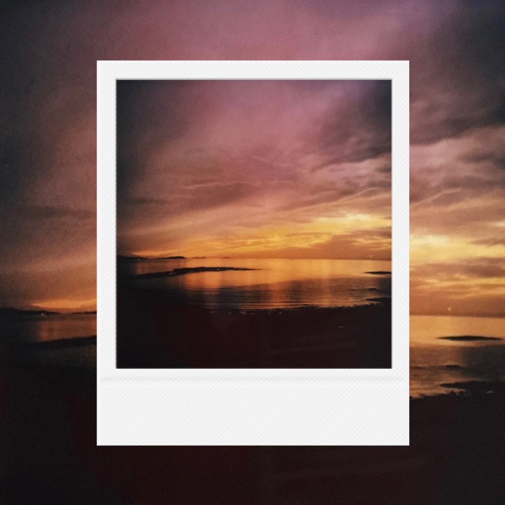 The breath of a silent sea within an analog film frame featuring golden sunset light breaking over a purple-hued horizon