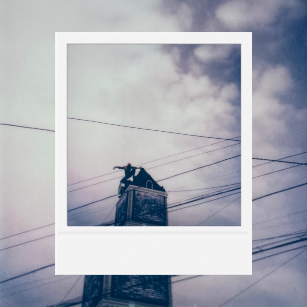 The lonely gaze of a hero standing precariously atop tangled urban wires captured within an analog film frame