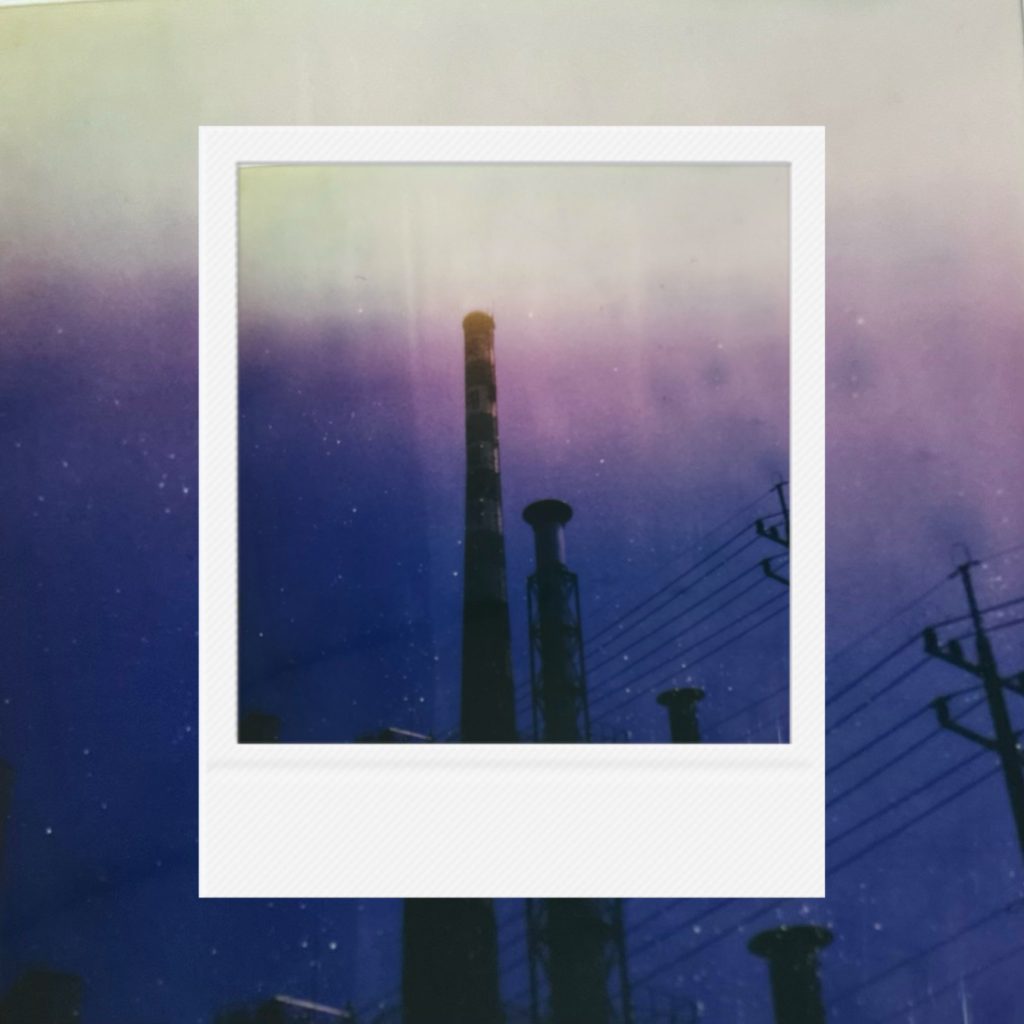 A quiet convergence of industrial silhouettes and fading light with a gradient transition into deep blue stillness and a solitary atmosphere of structure, sky, and lingering glow